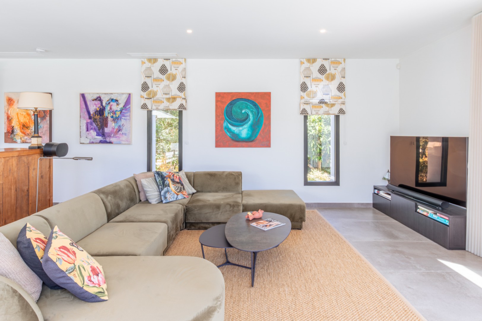 Modern living area featuring a large olive velvet sectional, natural jute rug, and minimalist TV console against a backdrop of vibrant contemporary art.