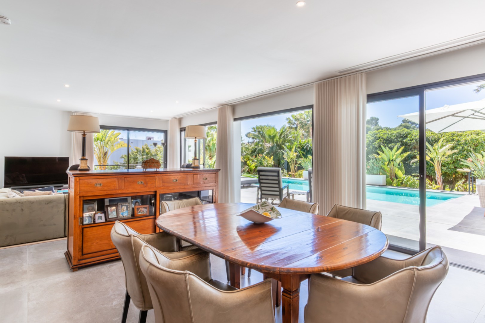 Open-plan dining space featuring a solid wood table and seamless access to the pool area through large sliding glass doors.