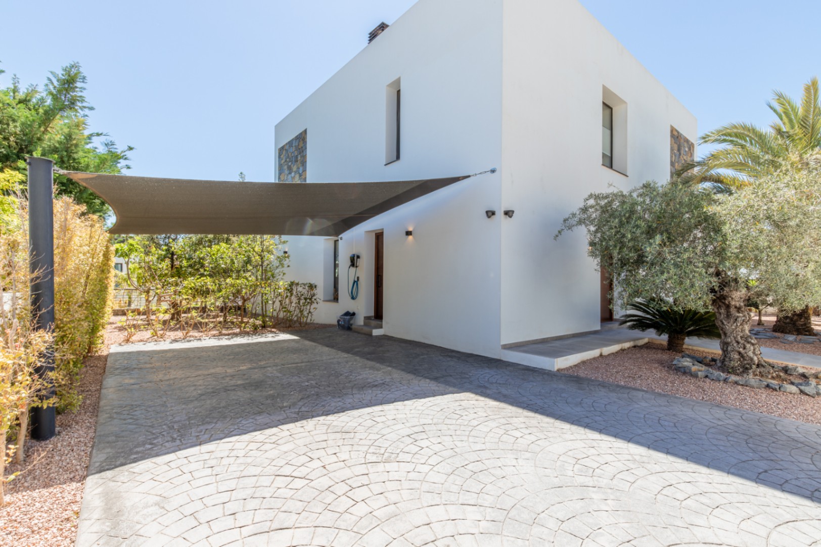 Parking area featuring stamped concrete, a large shade sail, and a wall-mounted EV charging station near the villa's side entrance.