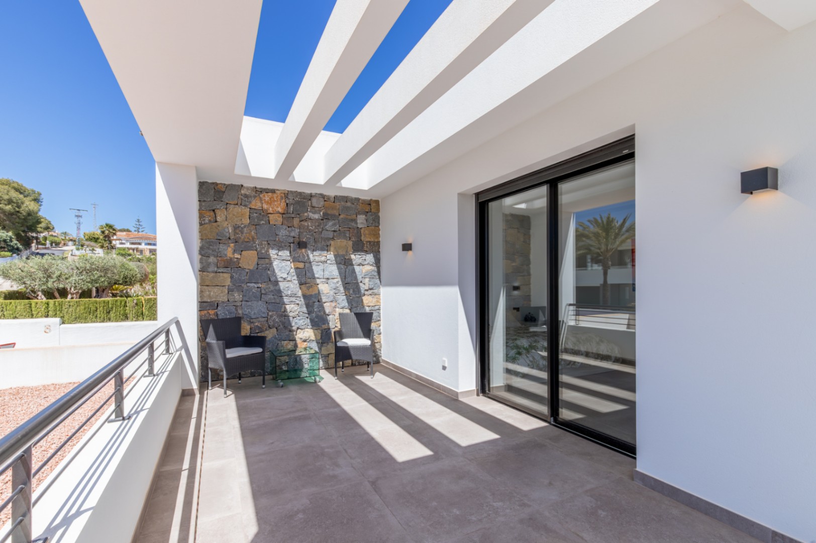 Private terrace featuring white pergola beams, a natural stone accent wall, and large sliding glass doors leading to the interior spaces.