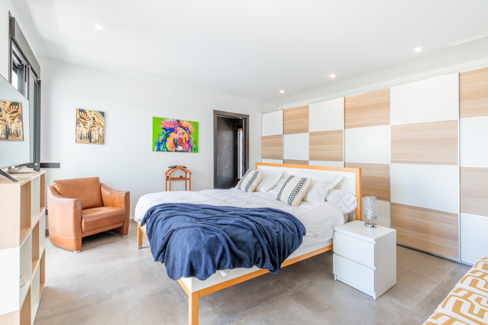 Spacious bedroom featuring a large built-in wardrobe with a checkered wood and white finish, grey tile flooring, and a contemporary leather armchair.