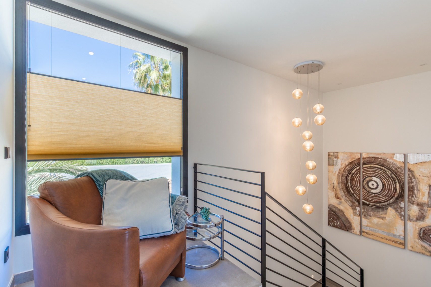 Upper floor landing featuring a cognac leather armchair, a cascading globe pendant light, and a large window with views of the Mediterranean palm trees.