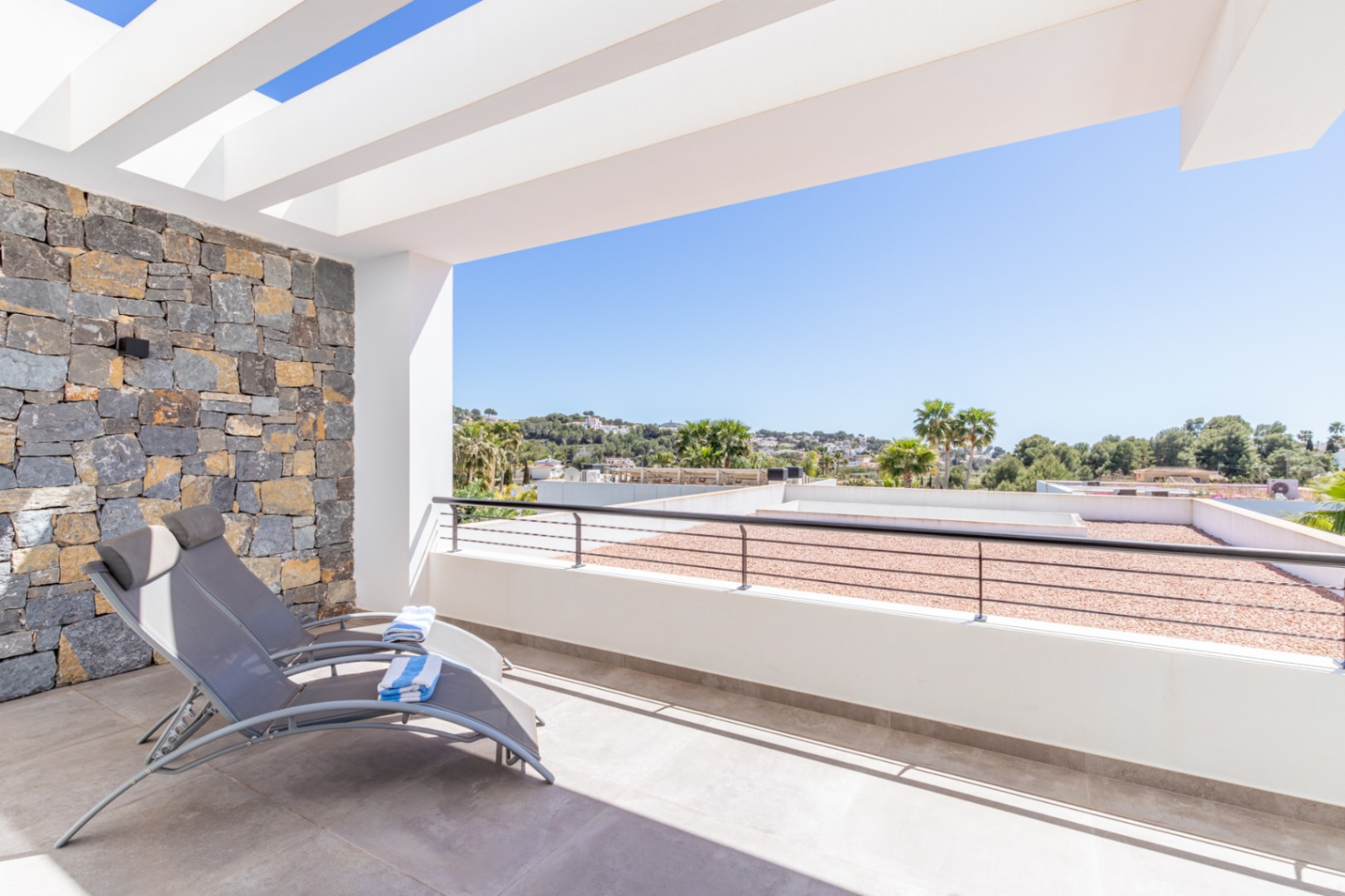 Upper-floor private terrace featuring a white pergola, natural stone accent wall, and open views of the Moraira landscape.