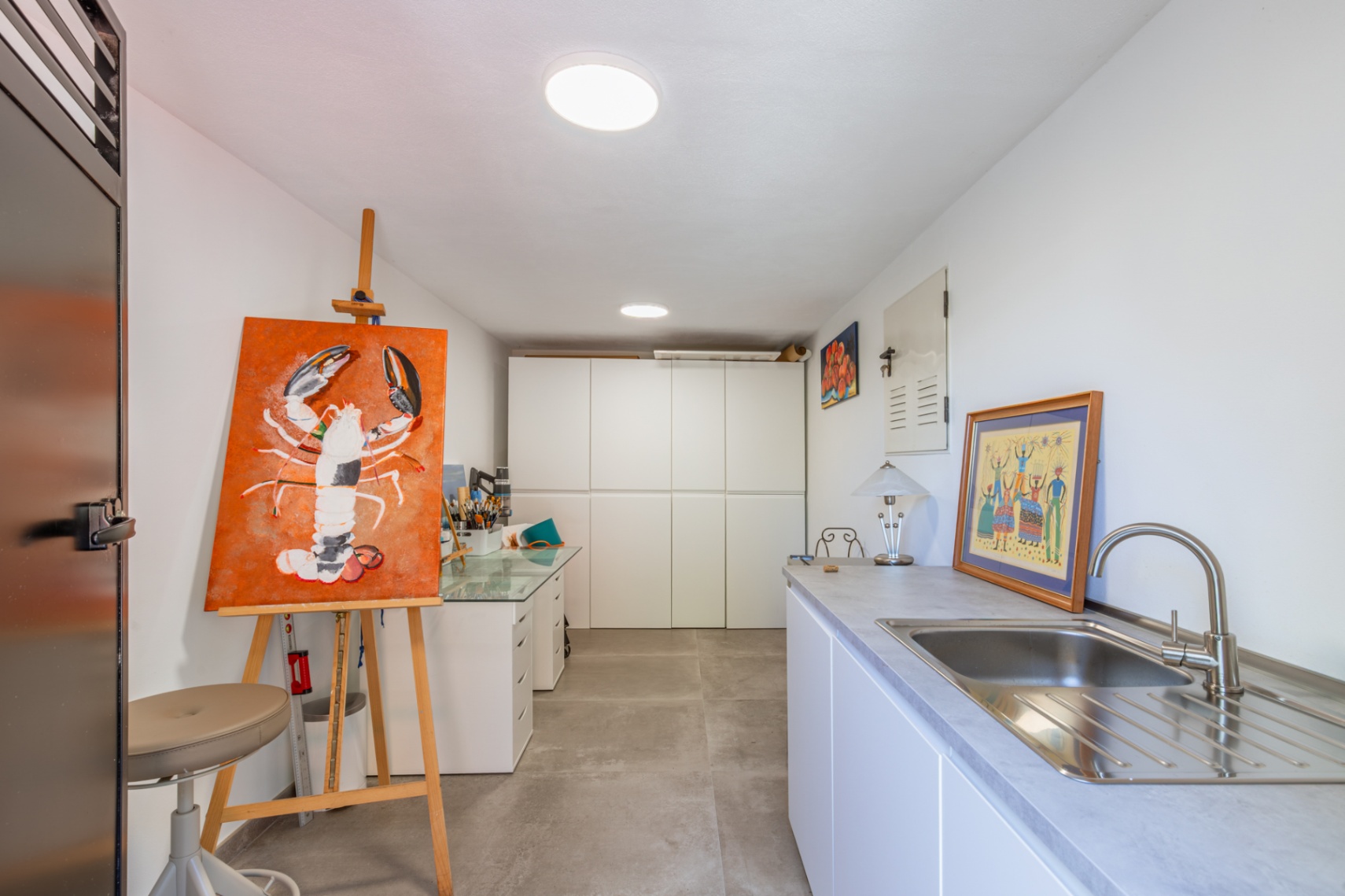 Versatile studio or utility space featuring white cabinetry, a stainless steel sink, and an art workstation set against grey porcelain floor tiles.