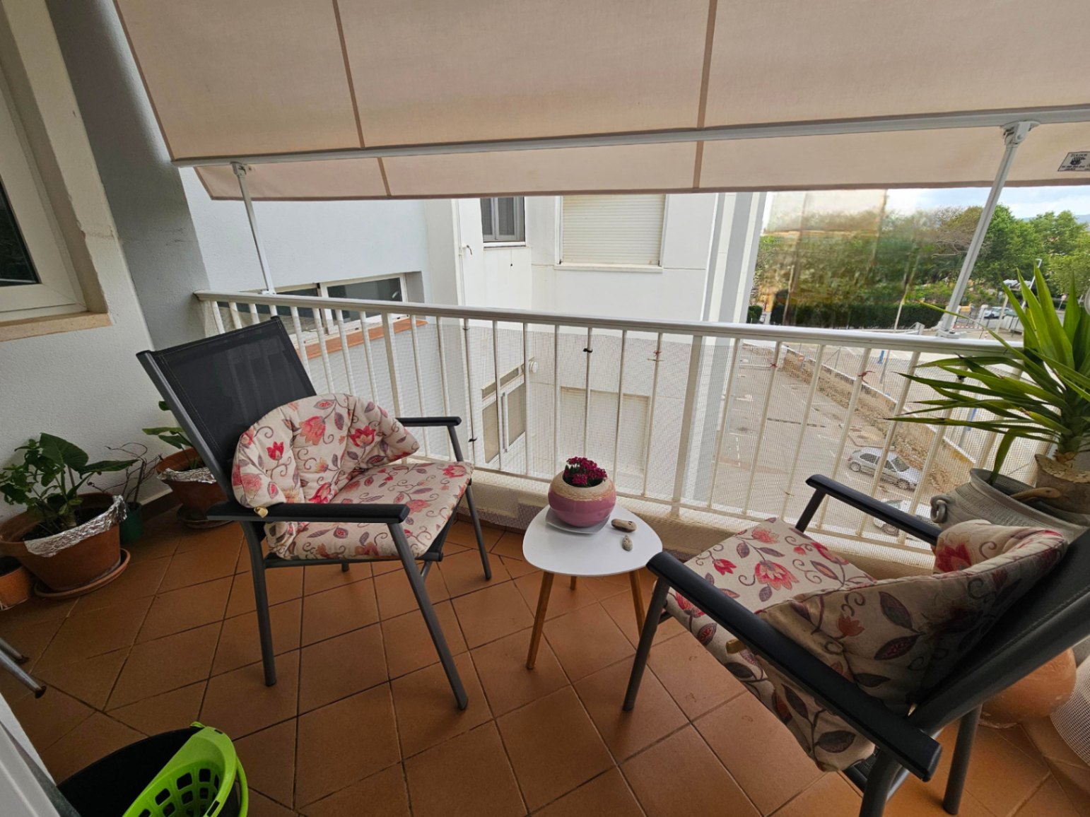 Balcony featuring terracotta tile flooring, a retractable awning for shade, and outdoor seating with floral cushions and a small side table.