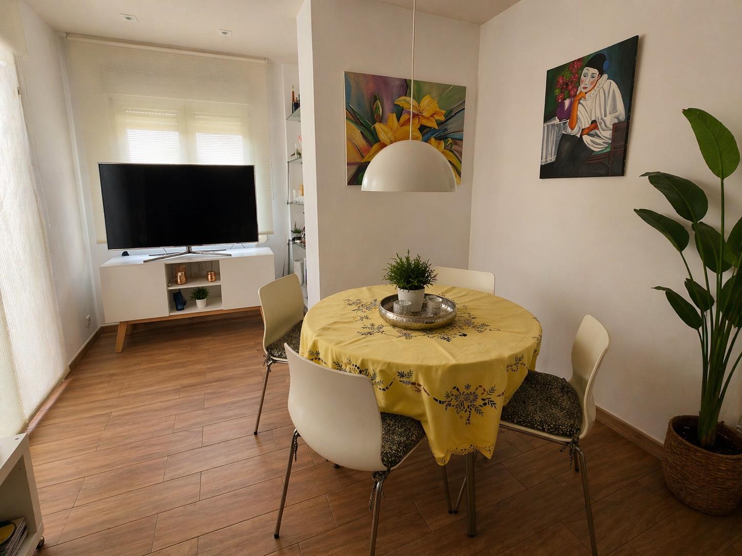 Bright dining area featuring a round table, white modern chairs, and wood-effect flooring, situated adjacent to the media console and TV.