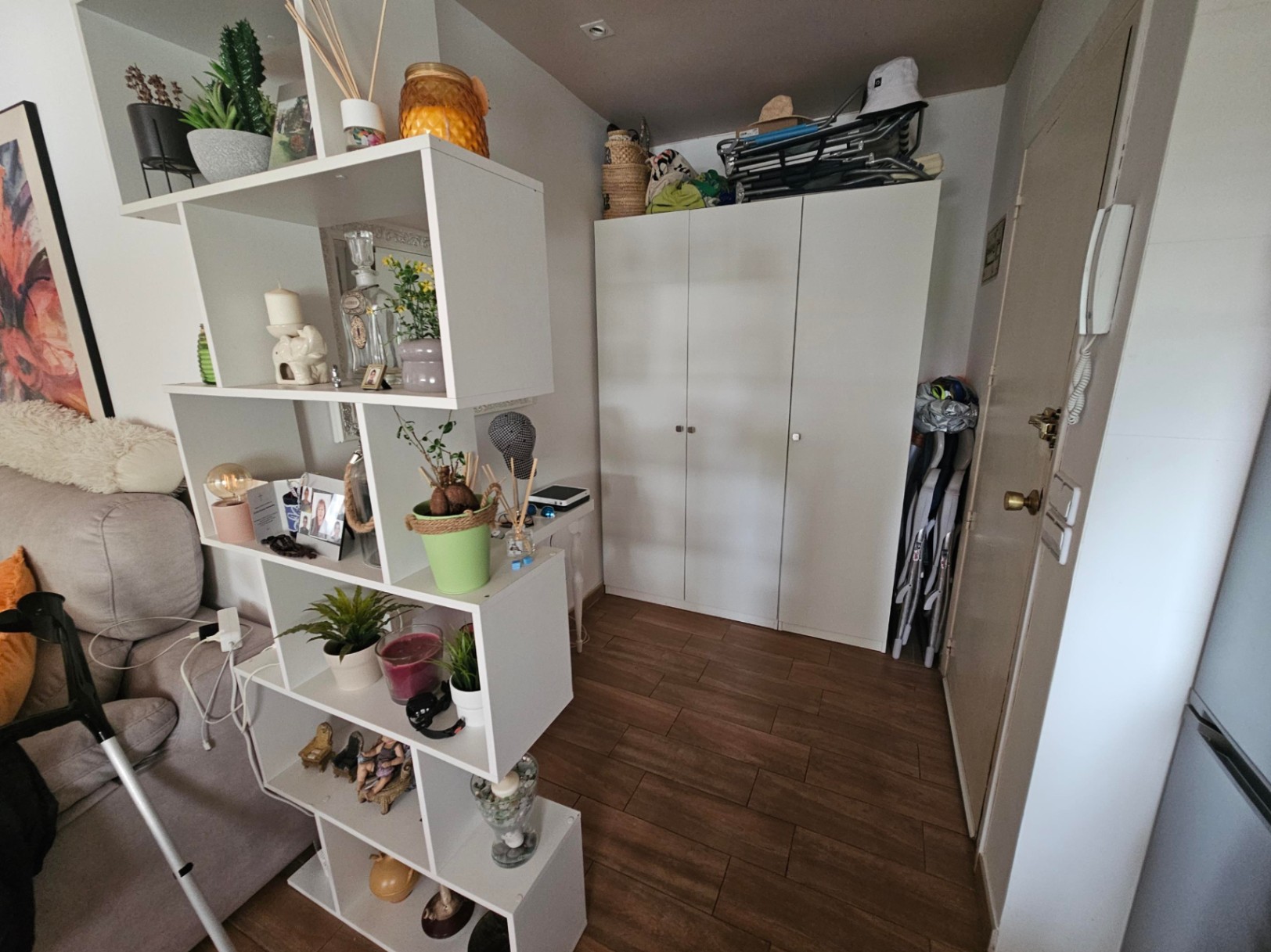 Entrance hall featuring wood-effect tile flooring, a white three-door wardrobe, and a modular shelving unit serving as a functional room divider.