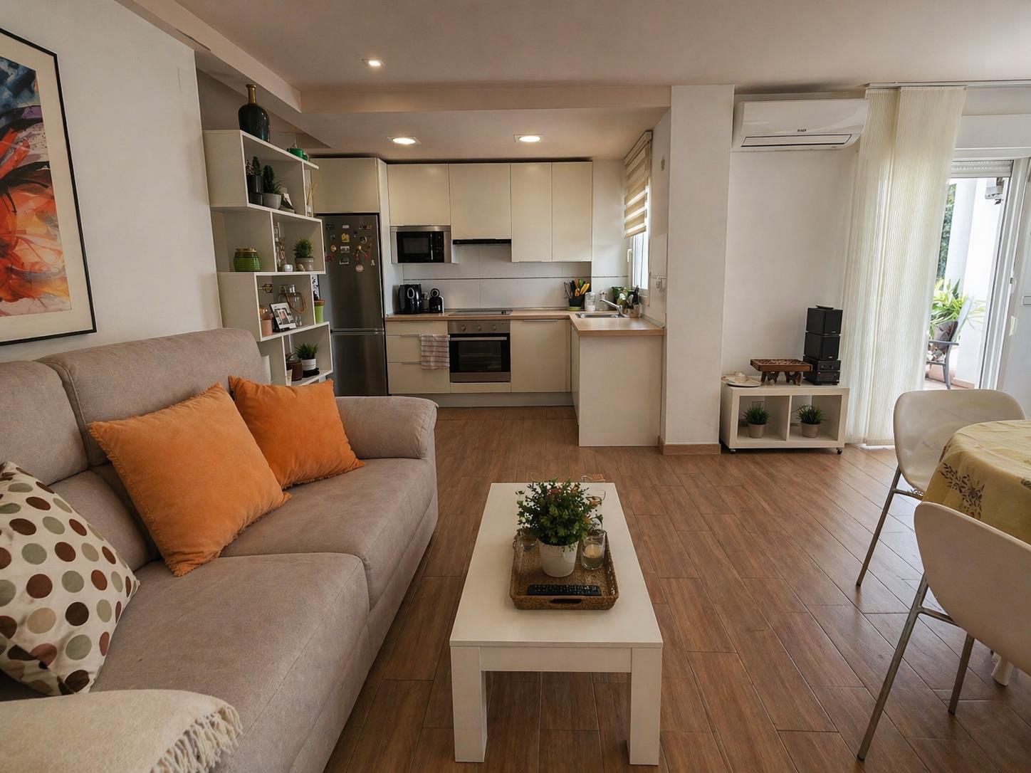 Open-plan living area featuring wood-effect flooring, a modern integrated kitchen with white cabinetry, and recessed ceiling lighting throughout the space.