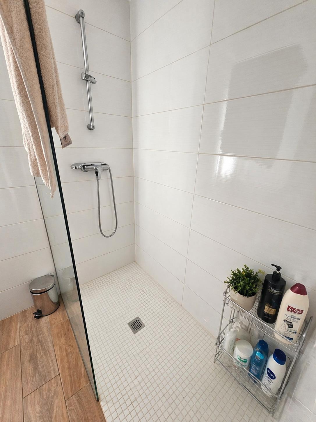 Walk-in Italian shower featuring a glass partition, horizontal white wall tiles, and a white mosaic floor. Includes chrome fixtures and adjacent wood-effect flooring.