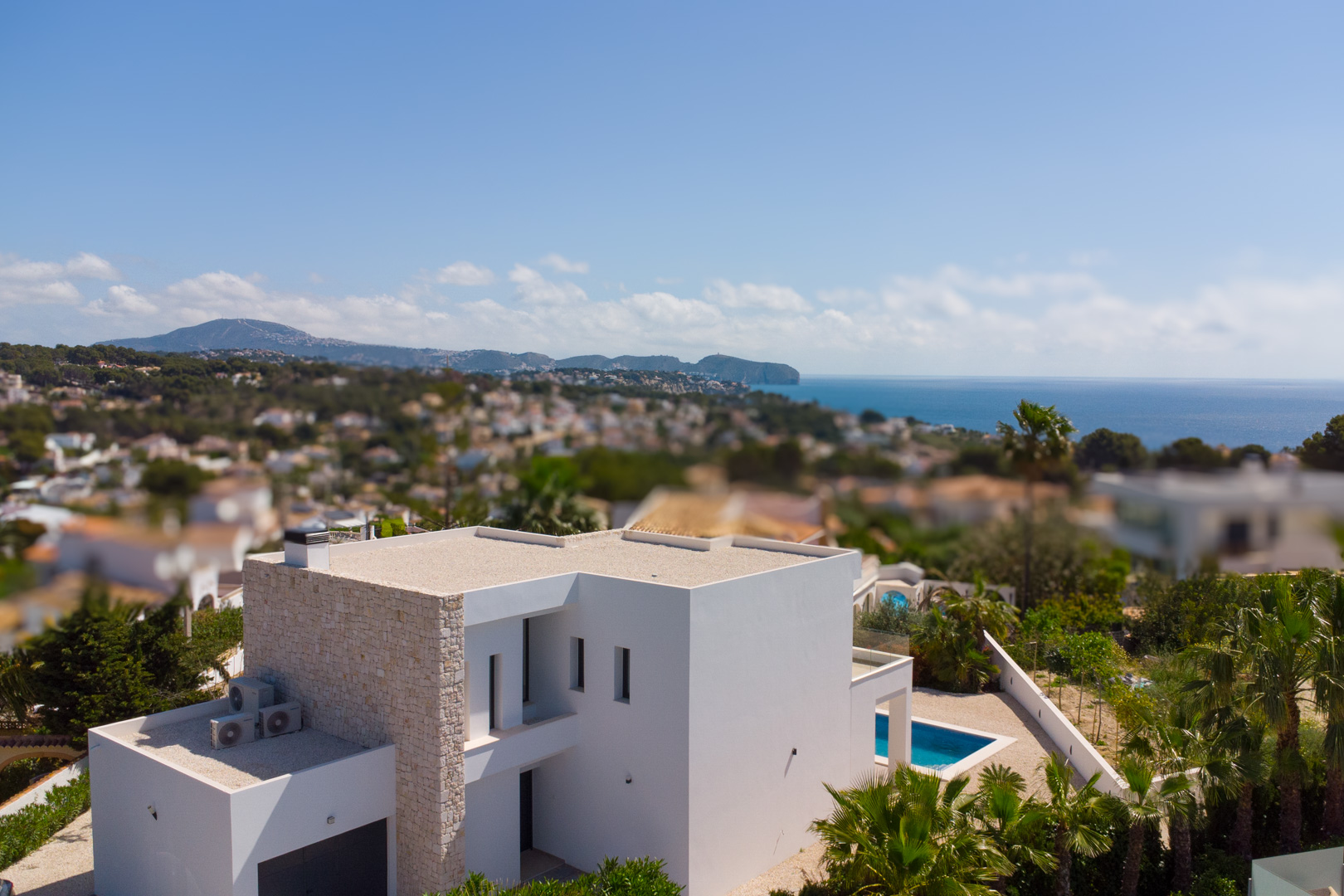 Aerial view of the modern villa featuring white facades, natural stone accents, a private swimming pool, and panoramic views of the Mediterranean coastline.