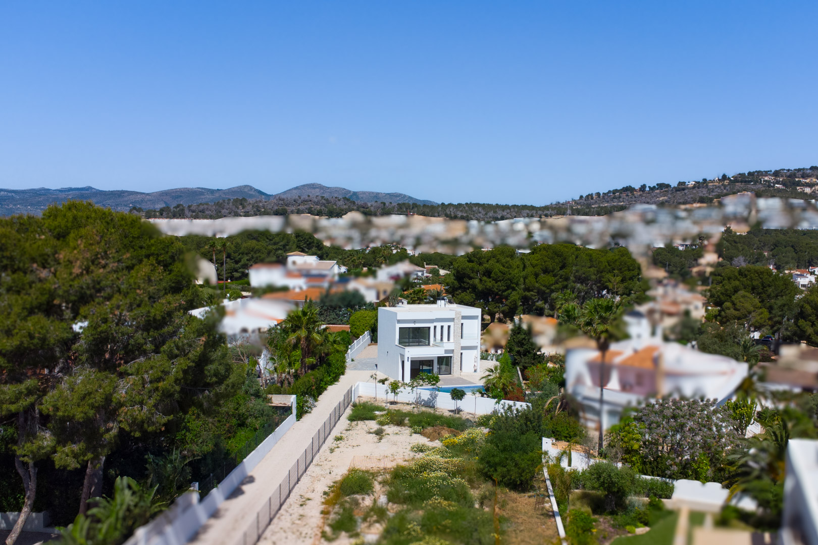 Aerial view of the modern white villa situated on an expansive flat plot, surrounded by Mediterranean pine trees and distant mountain ranges.