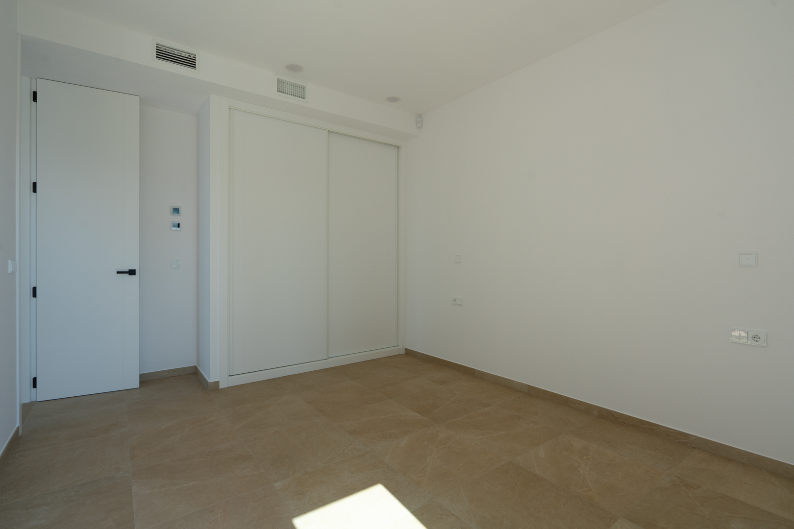 Bright bedroom featuring earth-toned porcelain flooring, a built-in wardrobe with white sliding doors, and integrated ducted air conditioning.