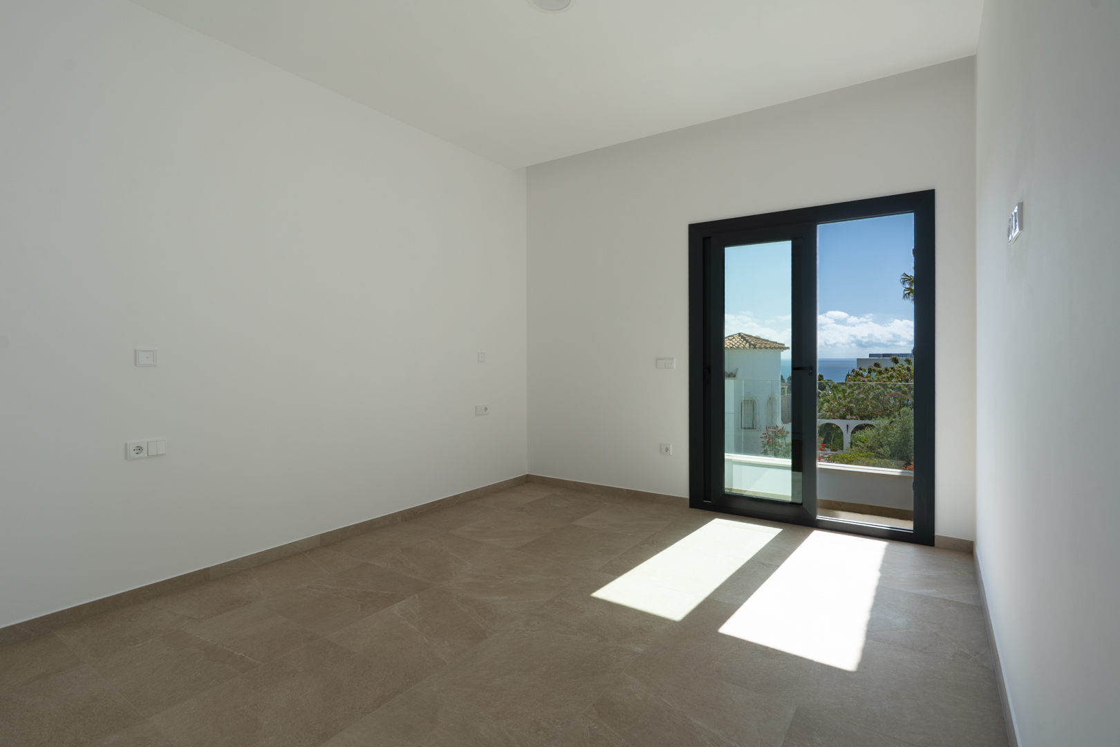 Bright bedroom featuring large-format porcelain tiles and a sliding glass door that opens to a private terrace with Mediterranean Sea views.