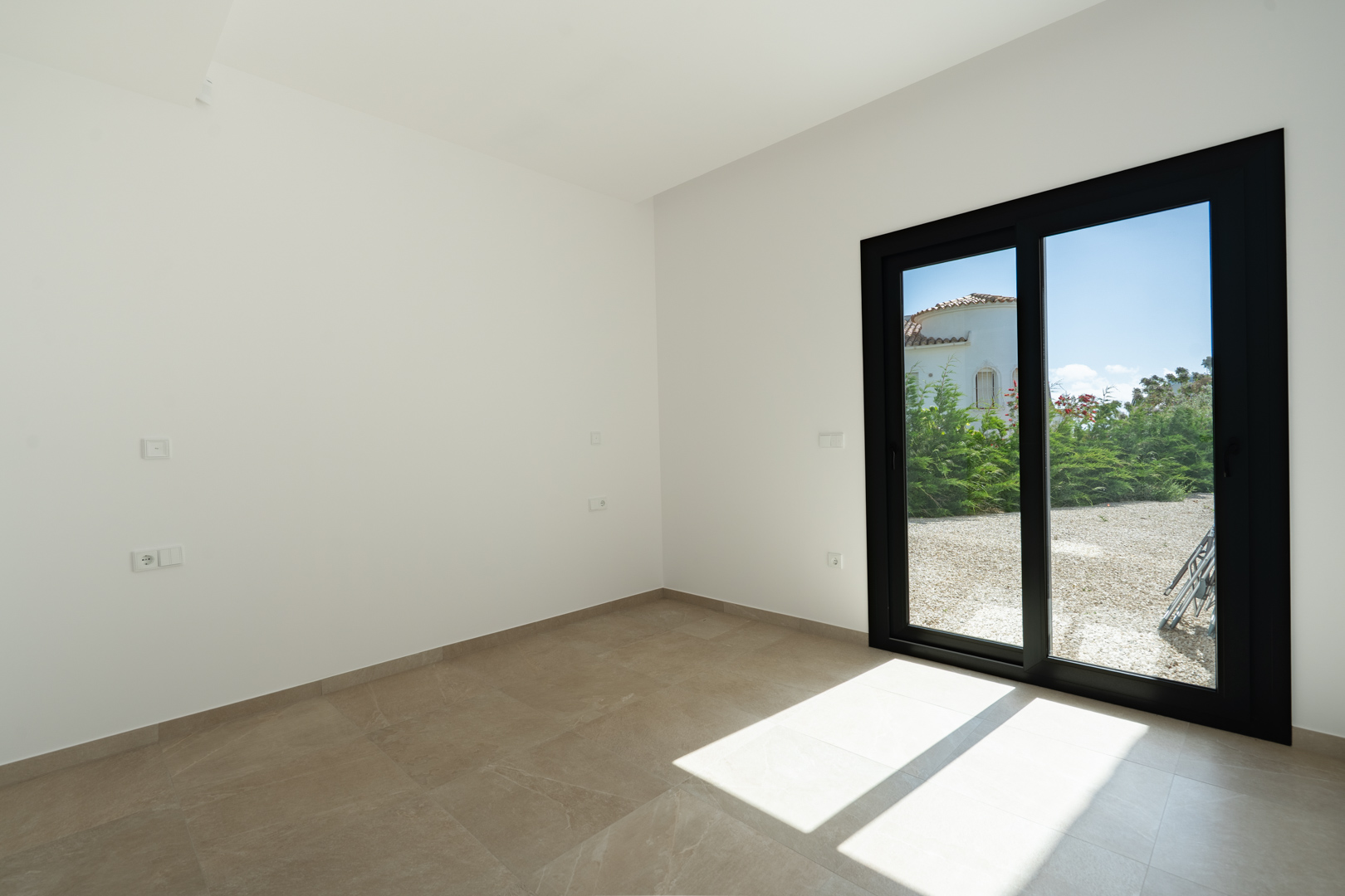 Bright interior featuring large-format porcelain floor tiles and a black-framed sliding glass door that opens onto the gravel garden area.