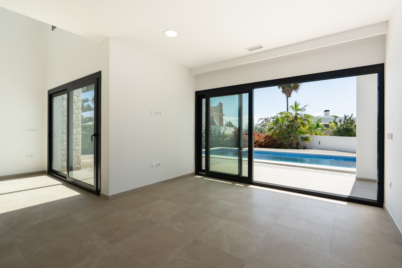 Bright living area featuring porcelain tile flooring and large black-framed sliding glass doors opening onto the terrace and swimming pool.