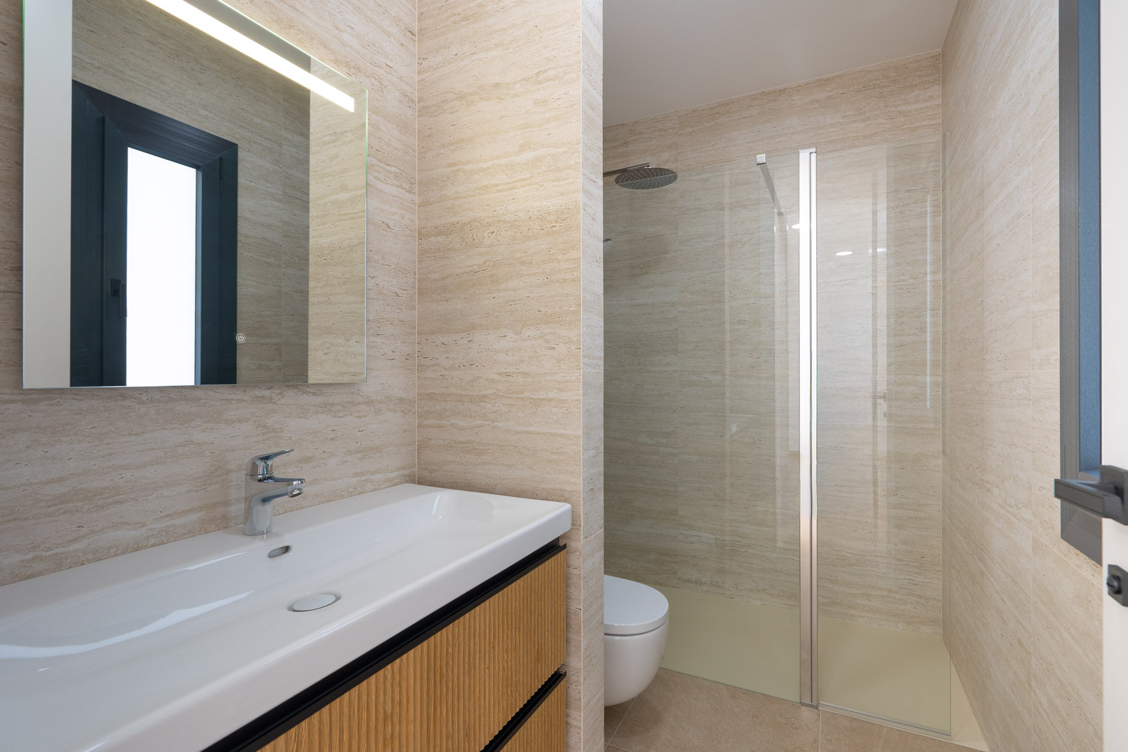 Designer bathroom featuring stone-effect porcelain tiling, a wall-mounted vanity with ribbed wood detailing, and a walk-in shower with a glass partition and rain shower head.