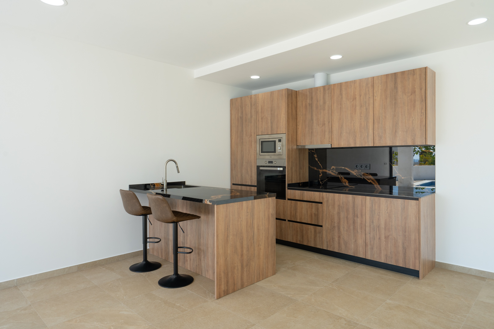 Designer kitchen featuring wood-finish cabinetry, black marbled countertops with gold veining, and a breakfast island with leather stools. Integrated appliances and recessed lighting.