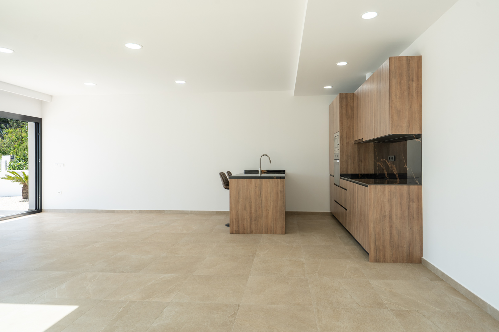 Designer kitchen featuring wood-finish cabinetry, dark veined countertops, and a central island, set within an open-plan space with large-format porcelain flooring.