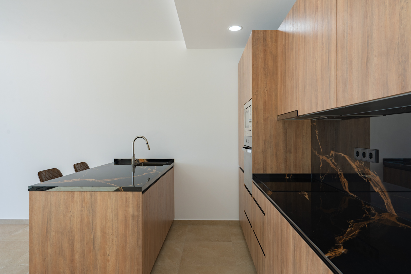 Designer kitchen featuring wood-finish cabinetry, dark veined stone countertops, and a central island with an integrated sink and minimalist faucet.