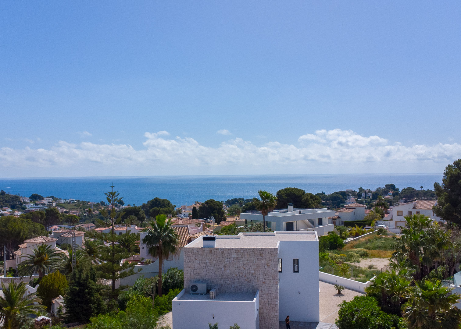 Elevated view of the villa's modern architecture with natural stone accents, showcasing panoramic Mediterranean Sea views and the surrounding greenery of Benissa.