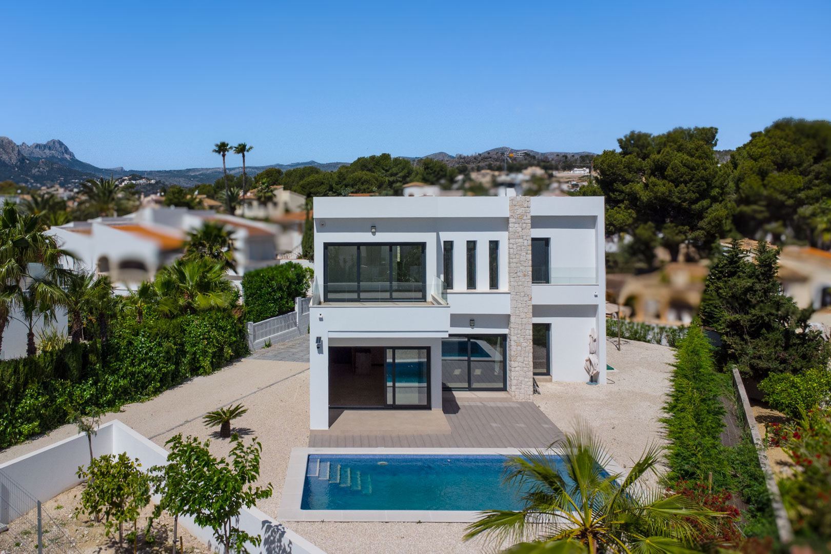 Exterior view of the modern white villa featuring a natural stone pillar, rectangular swimming pool, and terraces with glass balustrades.