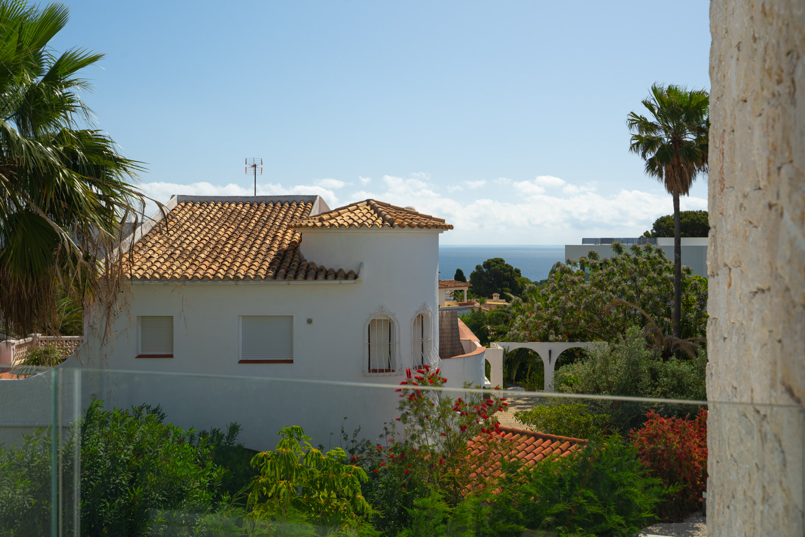 Mediterranean Sea views from the upper terrace, featuring a glass safety railing, natural stone masonry, and lush coastal vegetation.