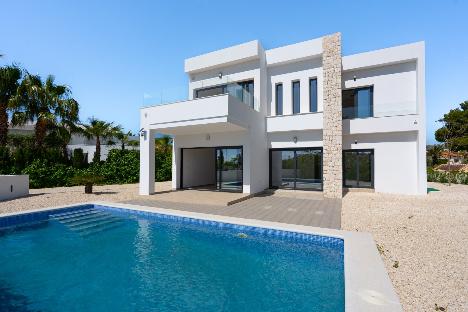 Modern two-story villa exterior featuring a natural stone accent wall, private swimming pool with integrated steps, and glass-railed terraces overlooking a gravel garden.