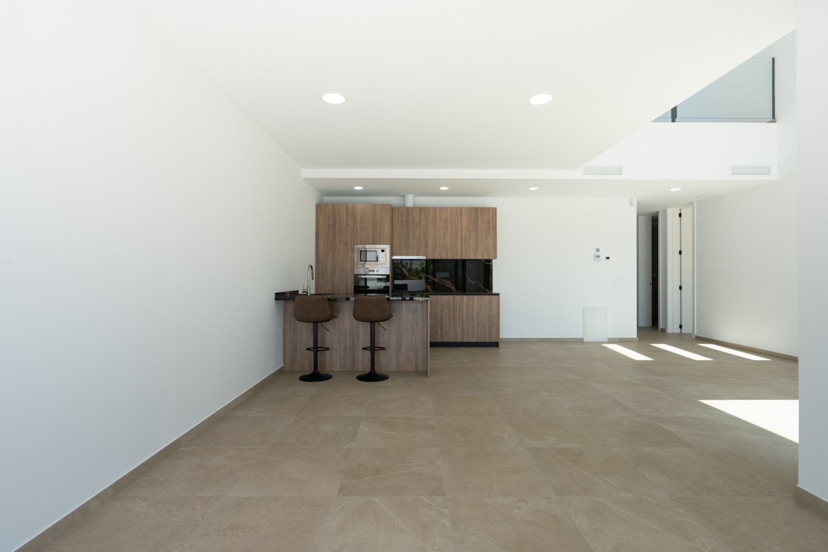 Open-plan designer kitchen featuring wood-finish cabinetry, dark stone countertops, and a breakfast bar, set within a spacious area with porcelain flooring and double-height ceilings.