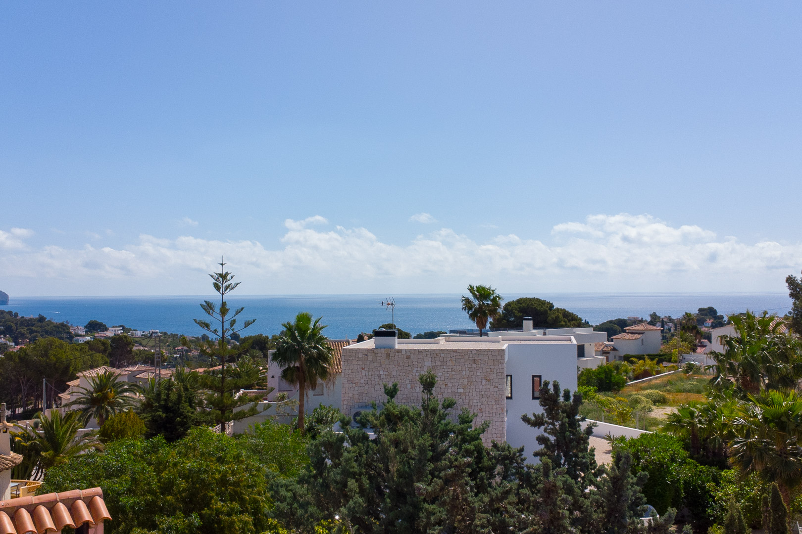 Panoramic view from the property overlooking the Mediterranean Sea, featuring white villa architecture and lush Mediterranean greenery under a clear sky.