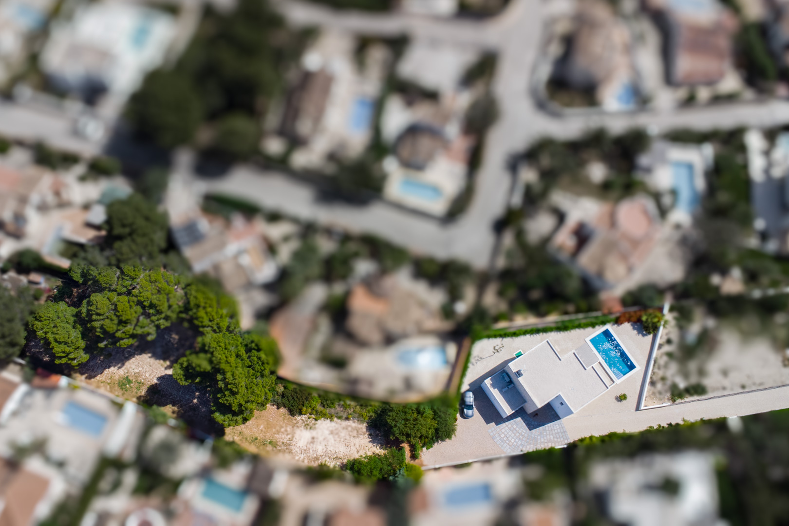 Top-down aerial view showing the modern white villa, the rectangular swimming pool, and the extensive flat plot surrounded by the residential landscape of Benissa.