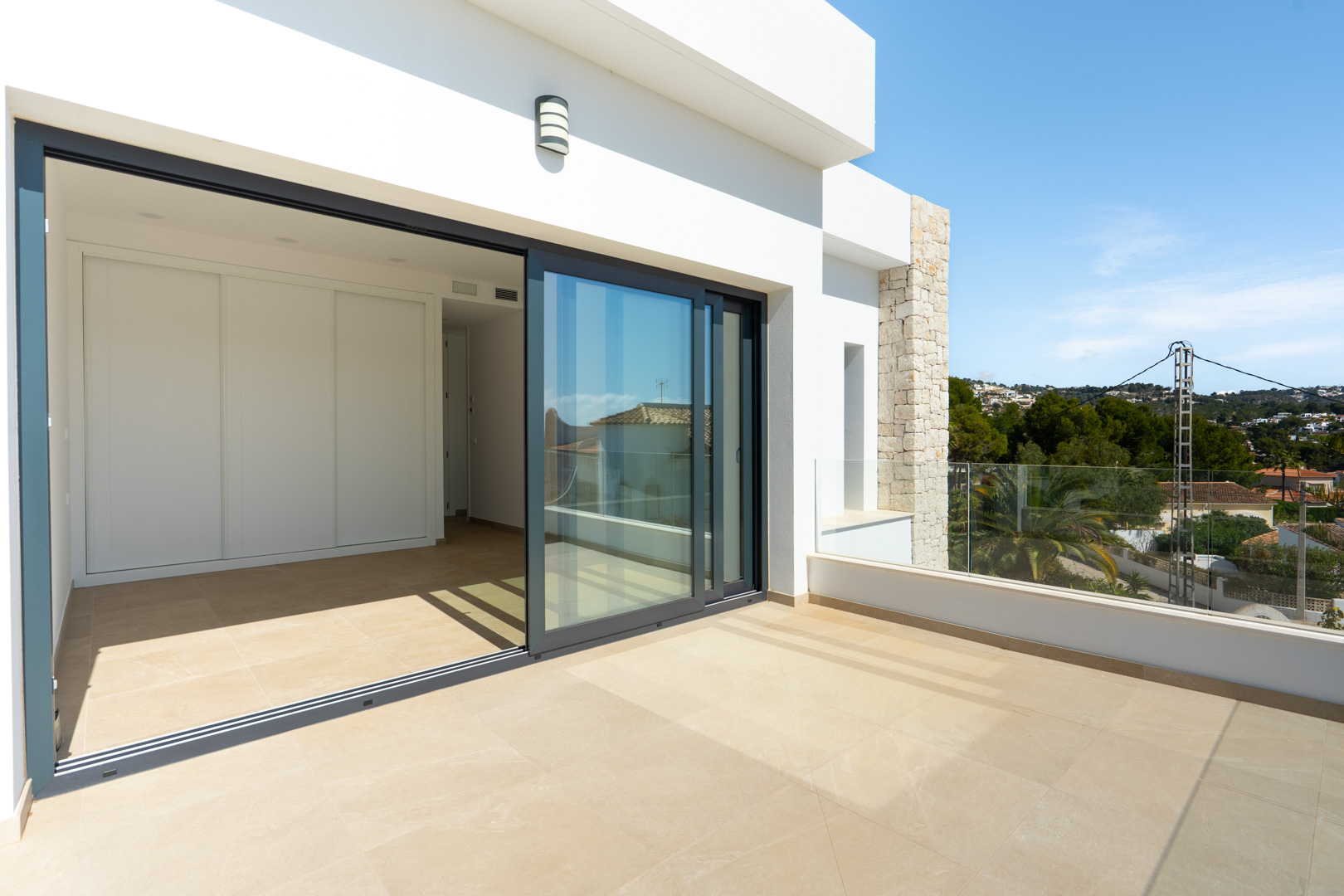 Upper floor terrace with porcelain flooring and glass balustrades, offering direct access to a bedroom with large sliding doors and built-in wardrobes.