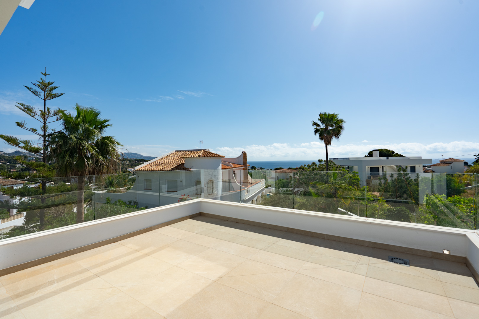 Upper-level terrace featuring large-format porcelain tiling and frameless glass railings, providing panoramic views of the Mediterranean Sea and local palm trees.