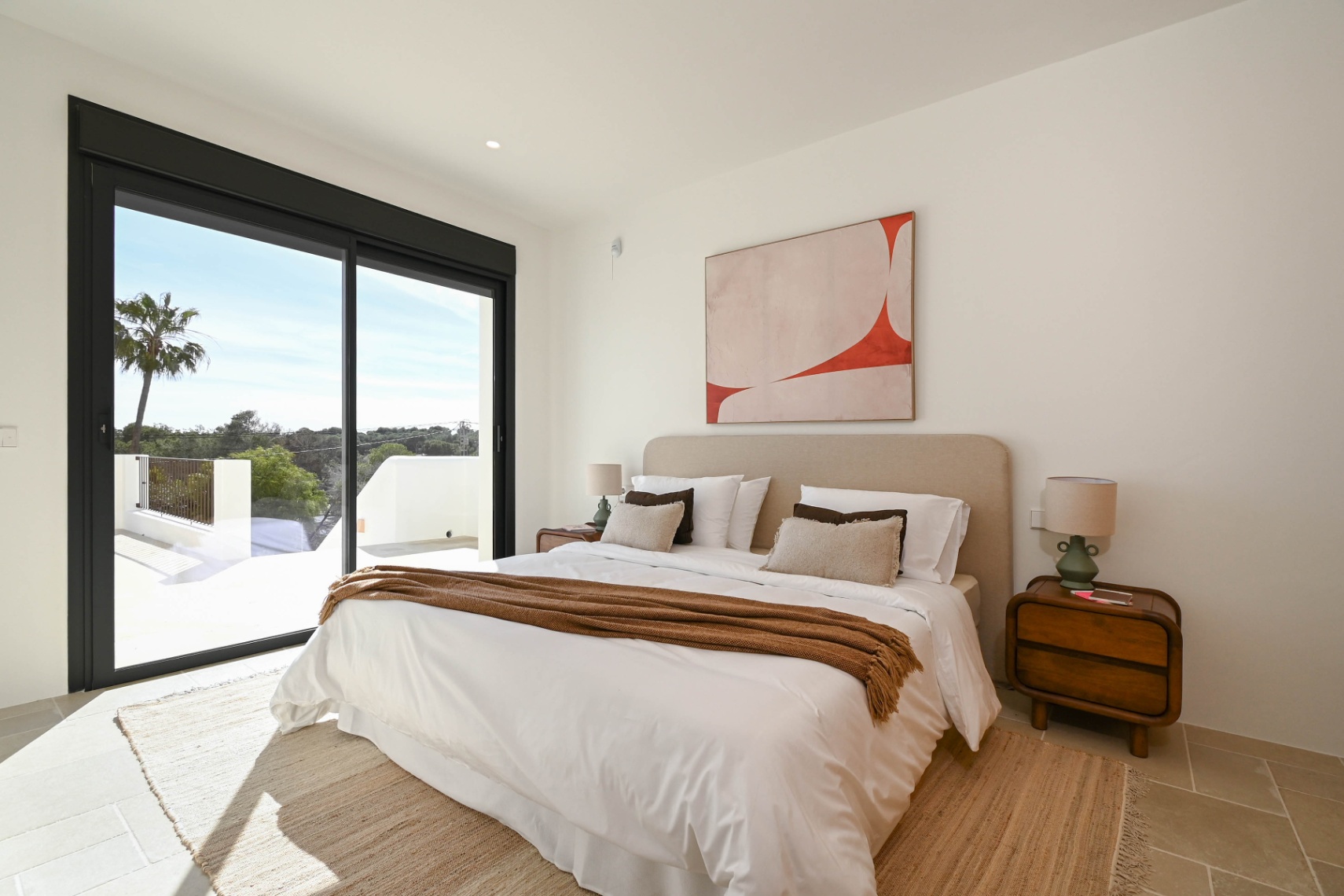 Bright bedroom featuring large black-framed sliding doors, direct terrace access, and natural stone flooring with neutral-toned decor.