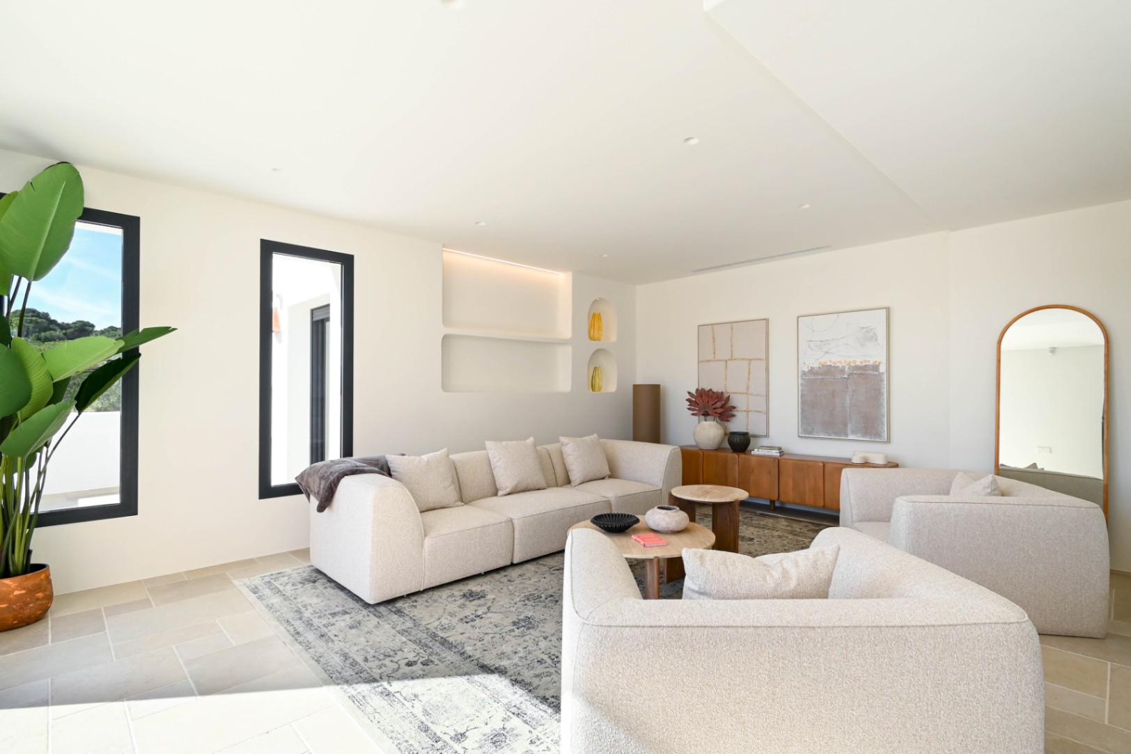 Bright living area featuring neutral-toned modular seating, integrated wall niches with LED lighting, and natural stone flooring under abundant natural light.