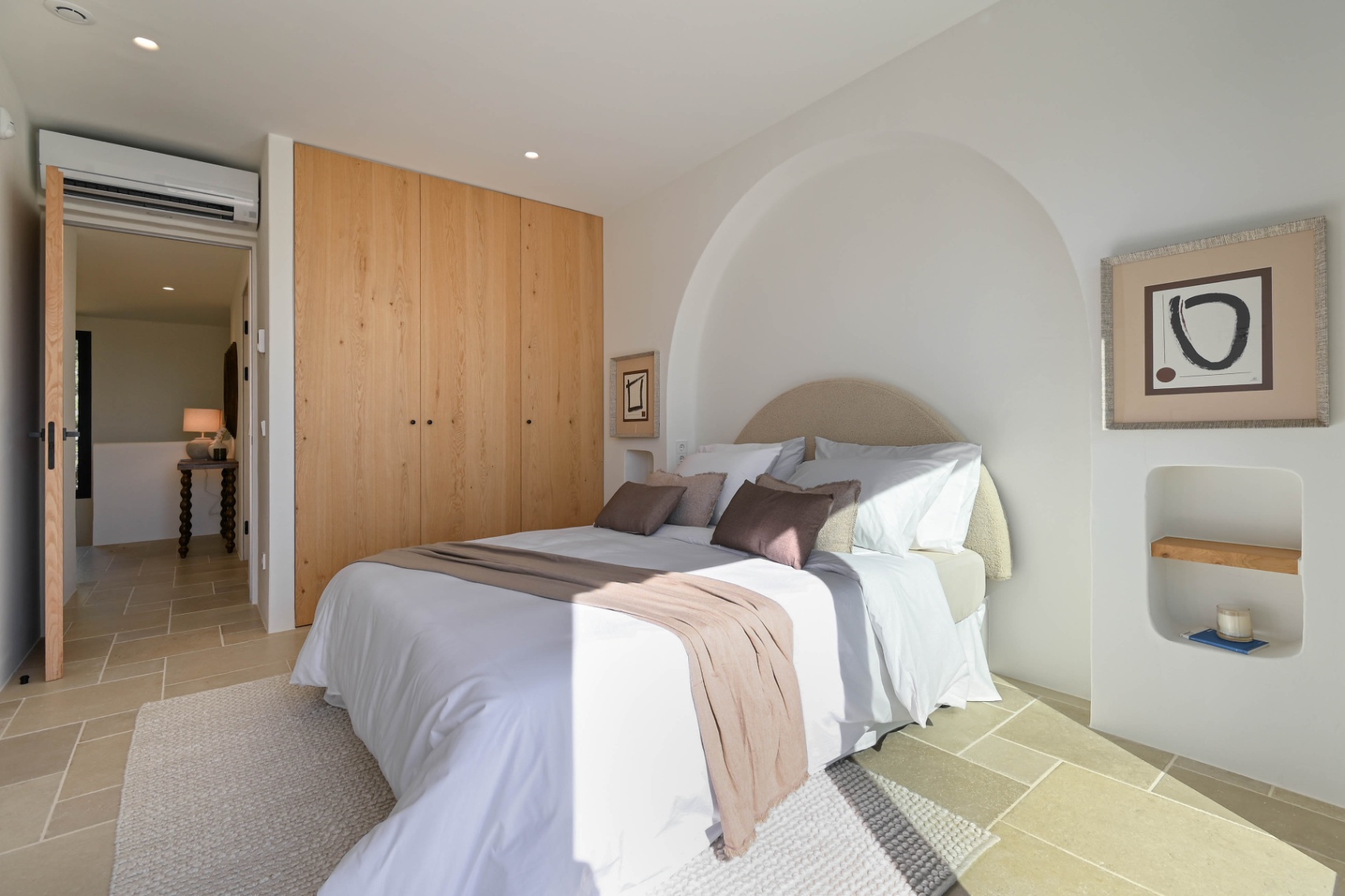 Modern bedroom featuring built-in oak wardrobes, natural stone flooring, and a unique arched wall alcove. Includes split-system air conditioning and recessed lighting.