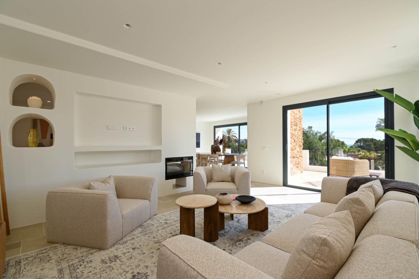 Modern living room featuring an integrated fireplace, minimalist recessed shelving, and large sliding doors connecting the interior to a sunny terrace.