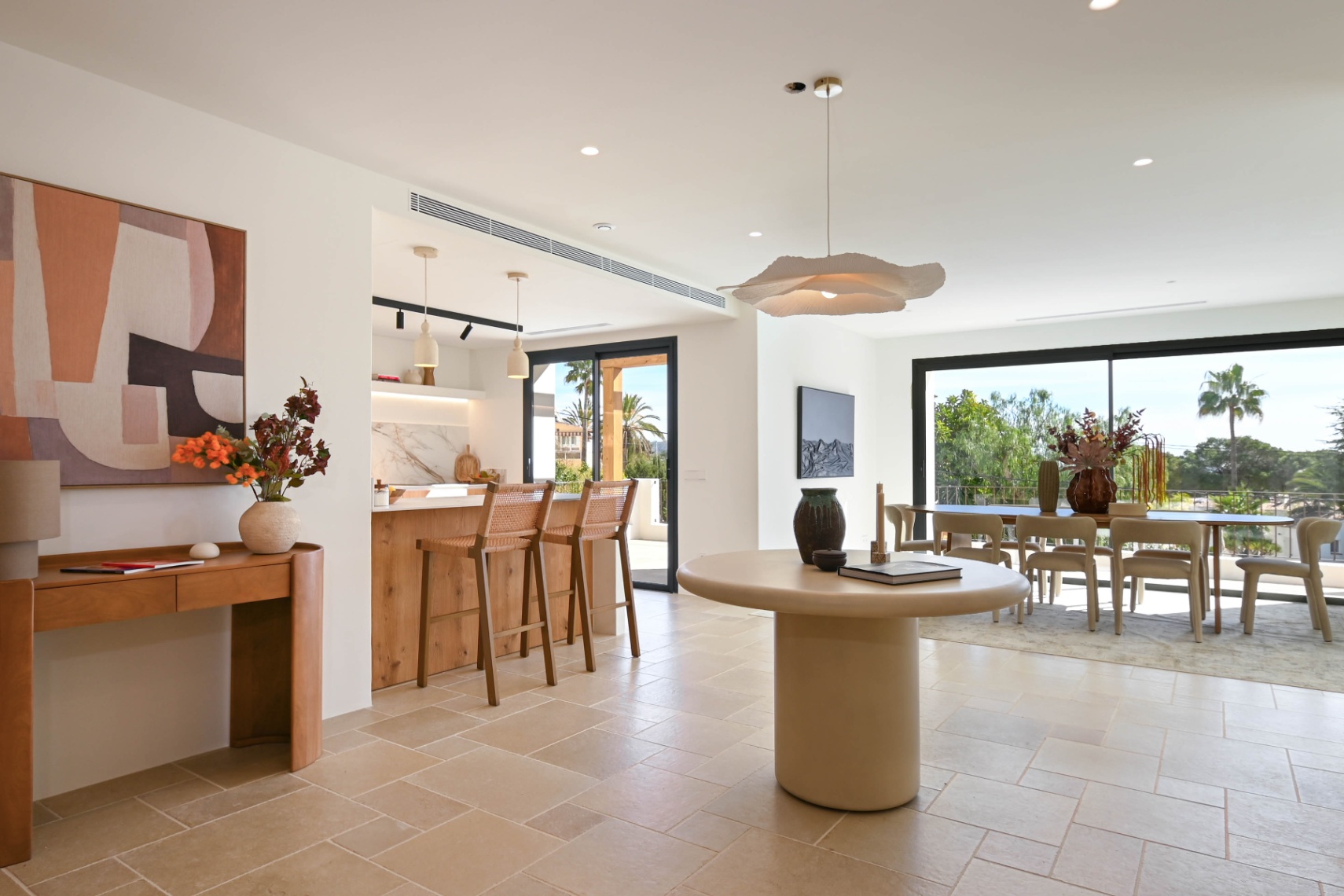 Open-concept living space featuring natural stone flooring, an integrated kitchen with a wooden island, and a bright dining area with large sliding glass doors to the terrace.