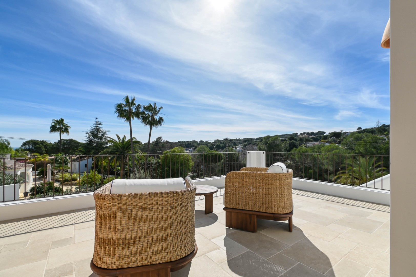 Upper terrace featuring natural stone tiling and woven lounge chairs, providing panoramic views of the Mediterranean landscape and palm trees.