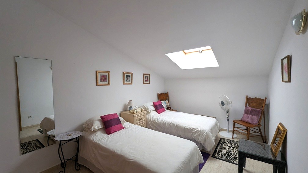 Attic-style bedroom featuring twin beds, a skylight for natural light, and neutral tiled flooring under a sloped ceiling.