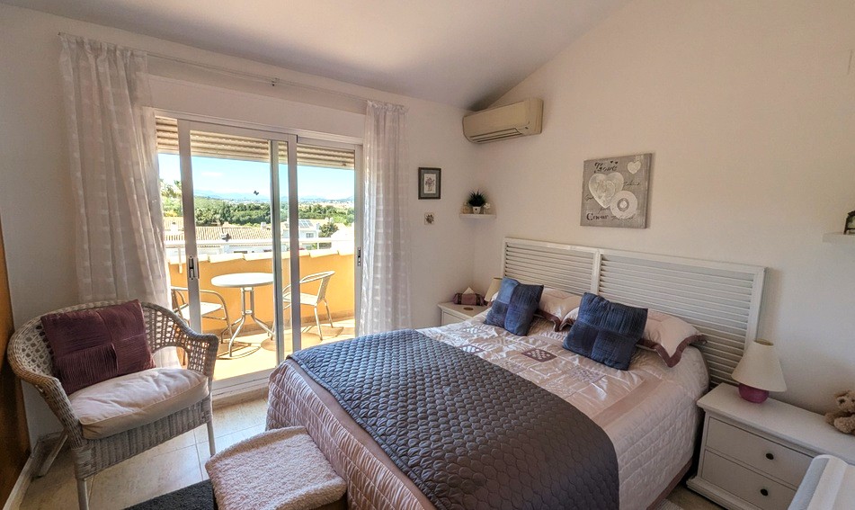 Bright master bedroom with a slanted ceiling, featuring a private terrace with mountain views, air conditioning, and a white slatted headboard.