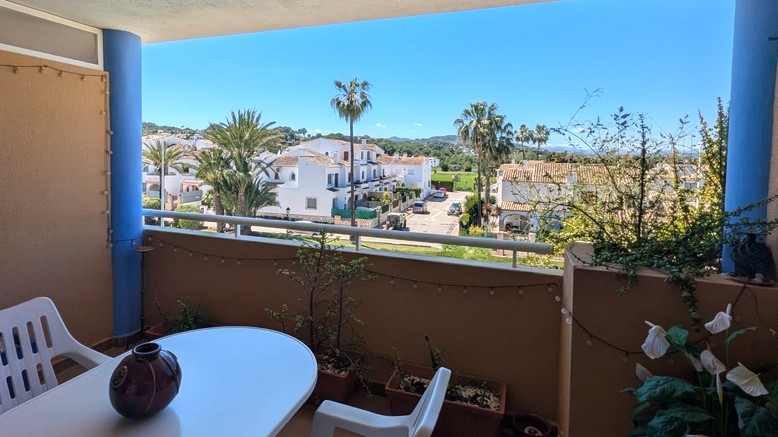 Covered terrace featuring a dining area with views of white Mediterranean villas, palm trees, and the Montgó mountain range.