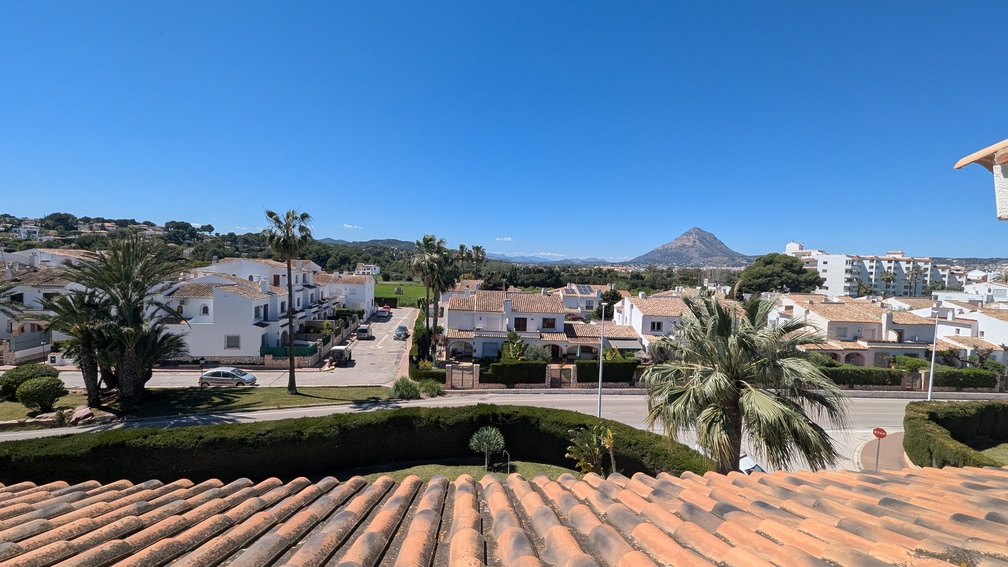Elevated view from the terrace over terracotta roof tiles, showcasing the residential neighborhood of Jávea and the iconic Montgó mountain in the distance.