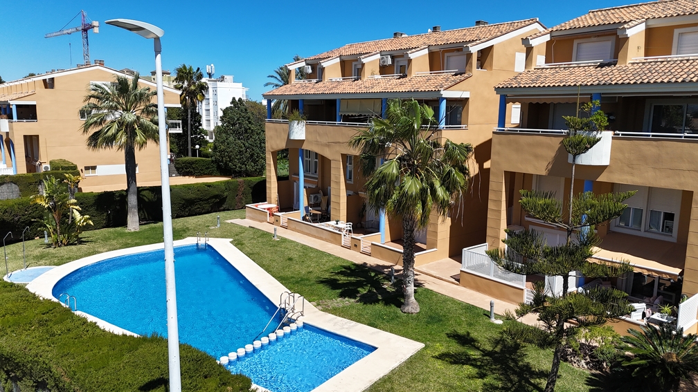 Elevated view of the communal pool area and lawn, showing the terracotta-toned facade with blue pillars and private terraces under a clear sky.