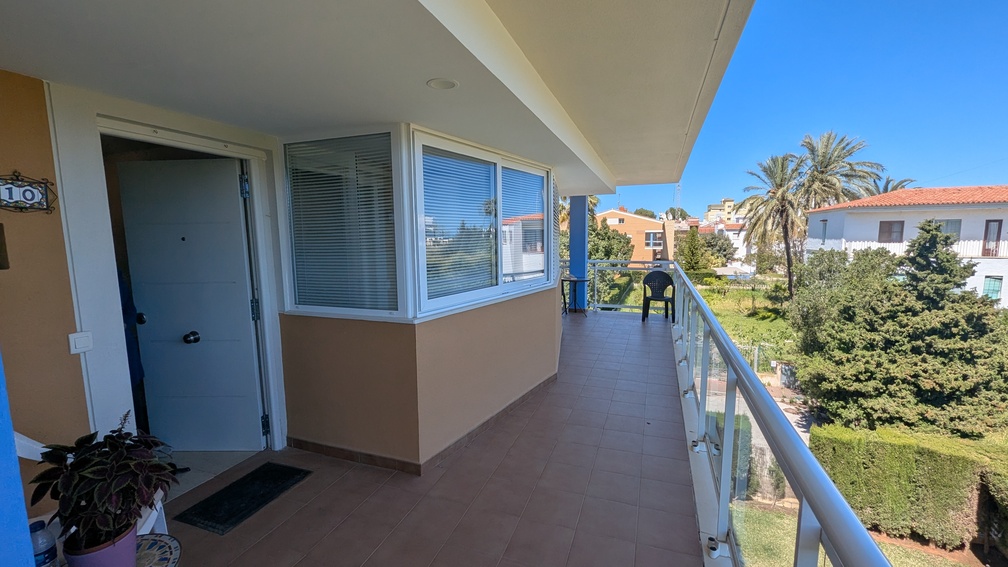 Entrance terrace with terracotta-style tiling and glass balustrades, offering views of the communal greenery and neighboring Mediterranean villas in Jávea.