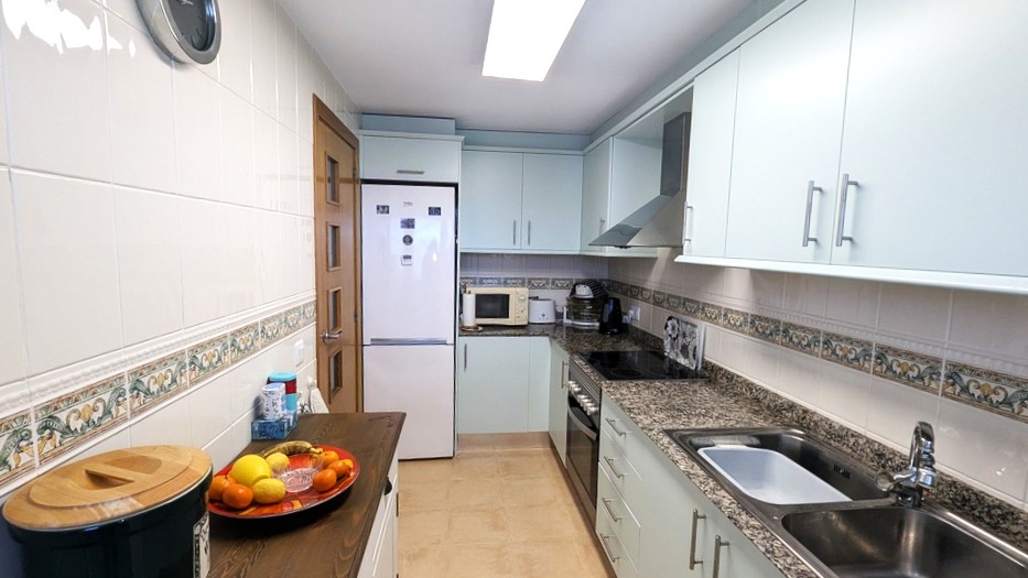 Fully equipped kitchen featuring light mint cabinetry, granite countertops, and white tiled walls with a decorative border. Includes a double stainless steel sink and integrated appliances.