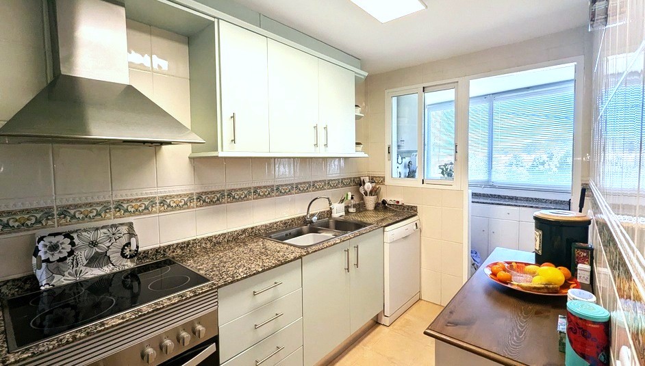 Fully fitted kitchen featuring granite countertops, a stainless steel extractor hood, and white cabinetry. A separate utility area is accessible through the rear window.