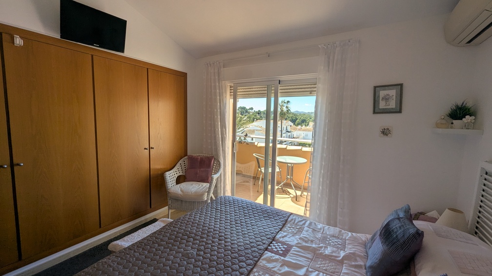 Main bedroom featuring a large wooden built-in wardrobe, air conditioning, and sliding glass doors opening onto a private terrace with scenic views.