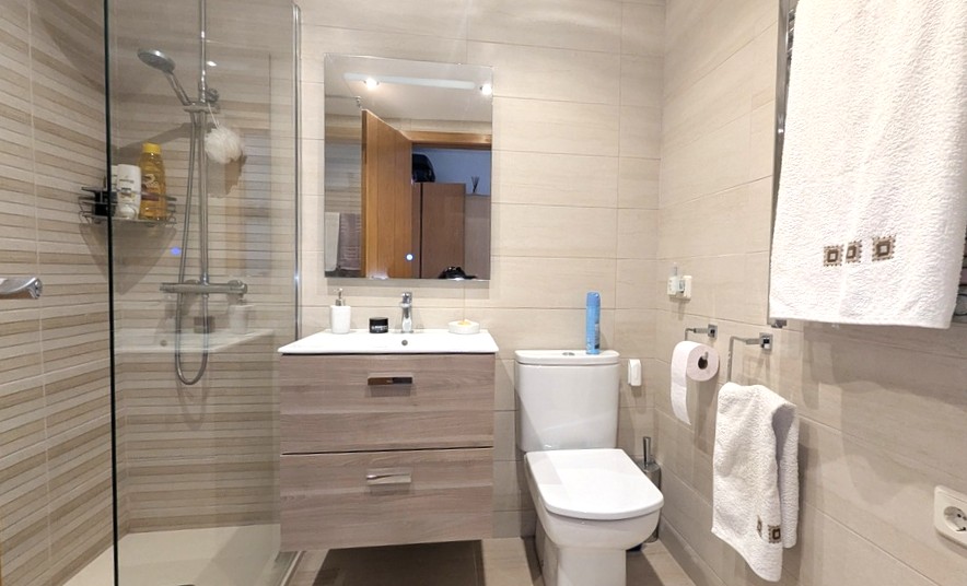 Modern bathroom featuring a walk-in glass shower, a floating light-wood vanity with dual drawers, and neutral horizontal tiled walls.