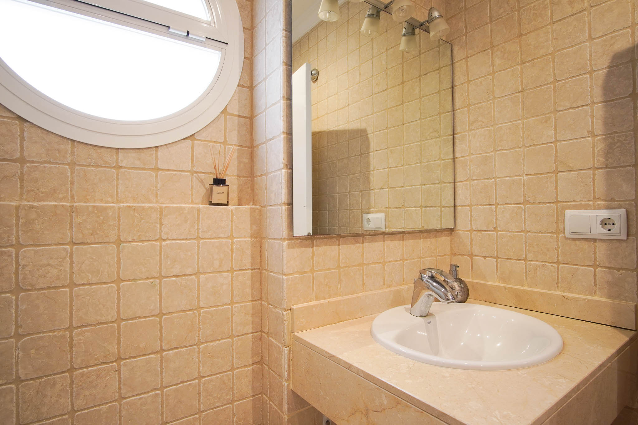Bathroom featuring tumbled marble wall tiles, a stone countertop with integrated sink, and a unique circular window providing soft natural light.