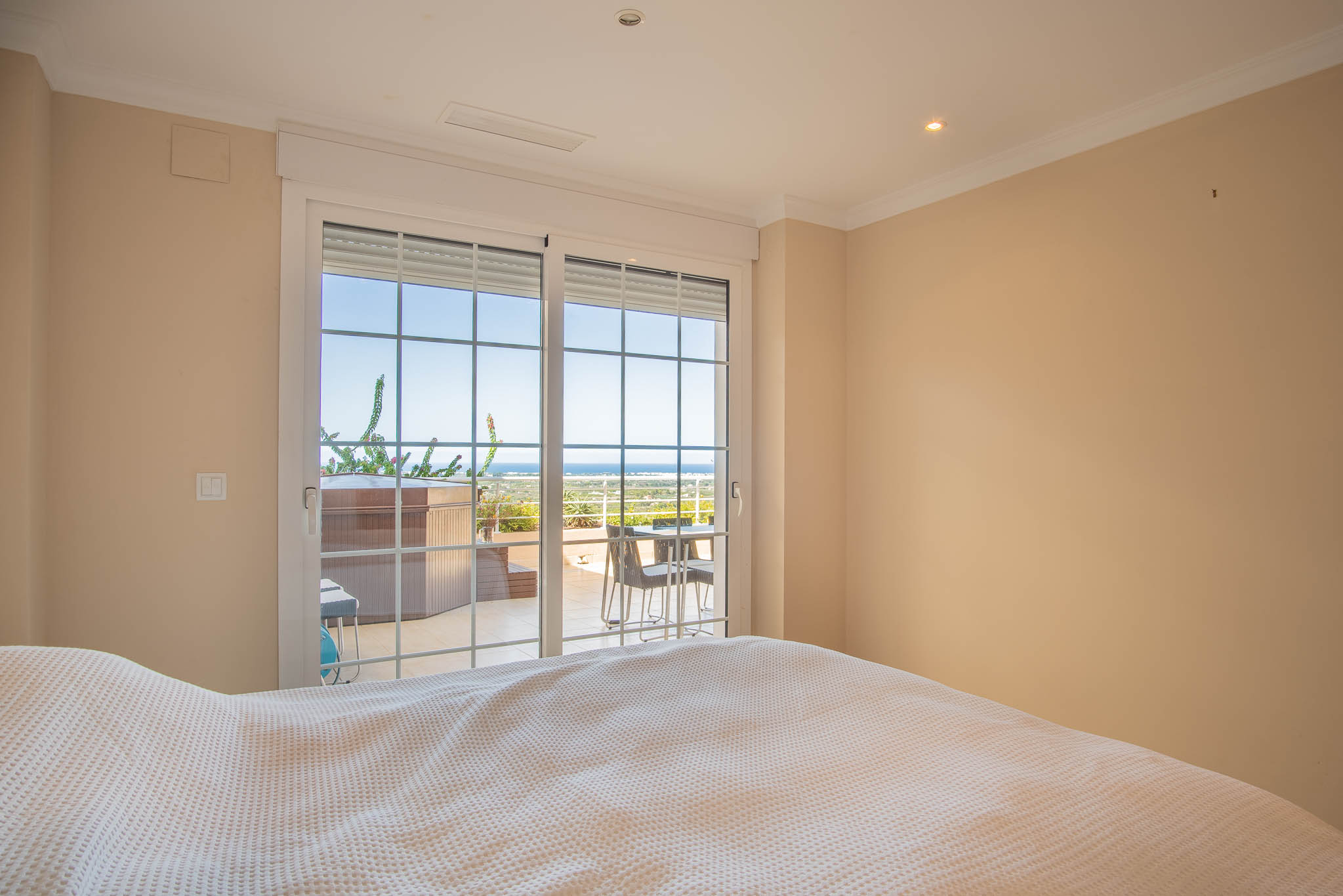Bedroom featuring sliding glass doors that lead to a terrace with a private jacuzzi. The space offers natural light and distant views of the Mediterranean coast.